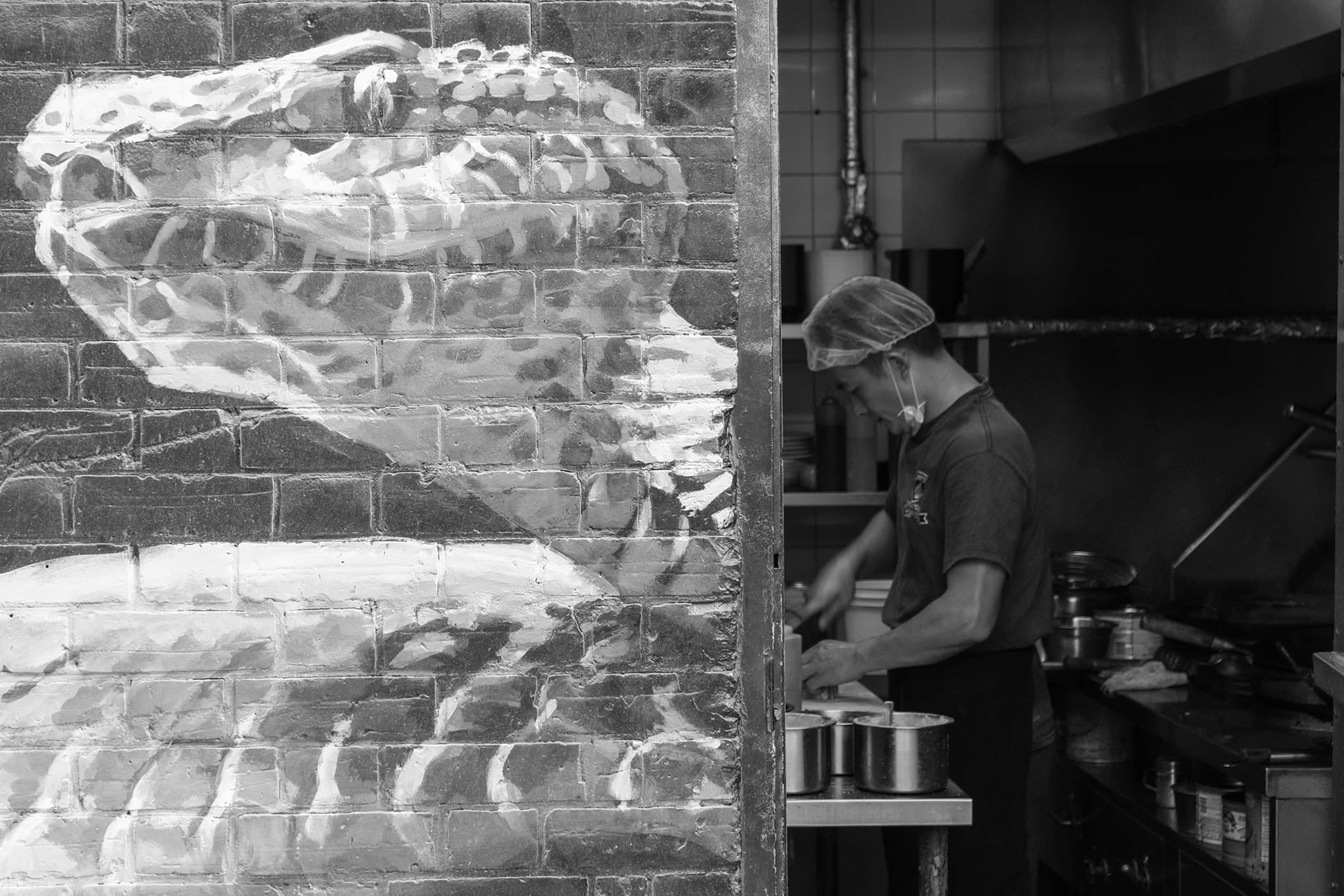 Street photograph: a cook at work beside a painted brick wall
